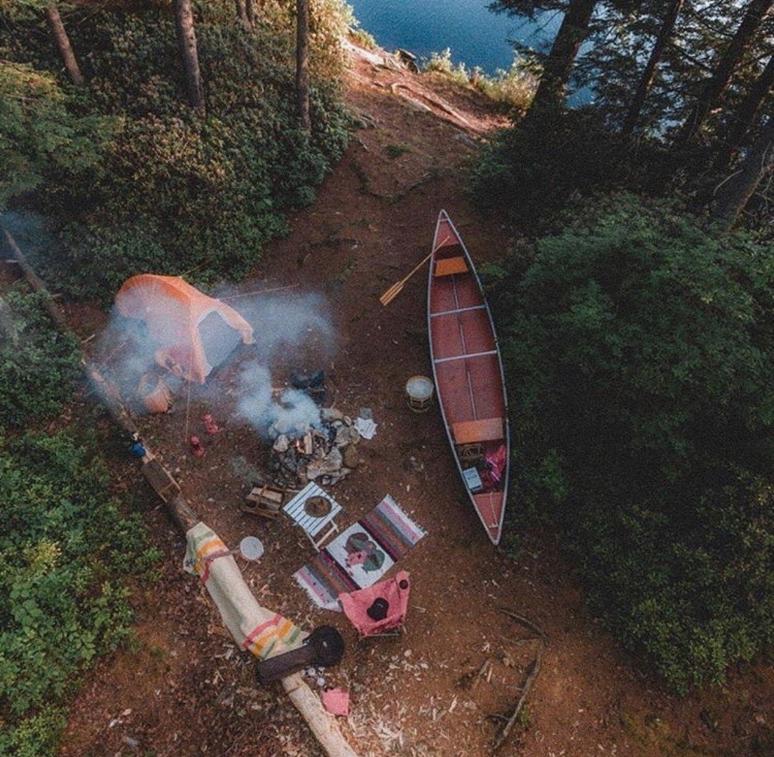 Campsite in the woods with a red canoe on a lake