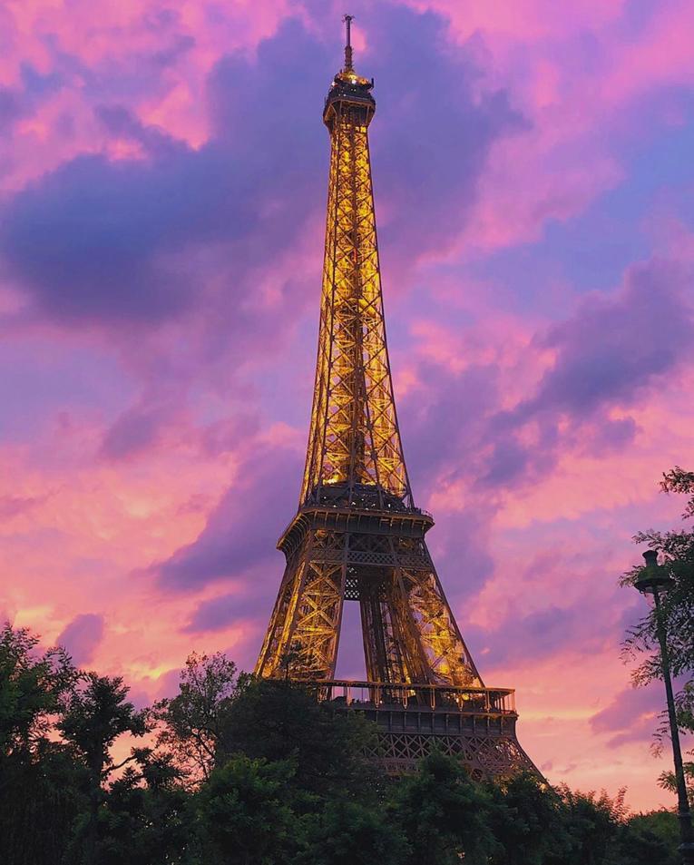 Eiffel Tower at sunset with Pink and purple sky. The tower is lit with yellow lights at twilight